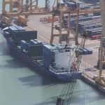 Photograph of a busy container port with cargo ships and cranes at sunset.