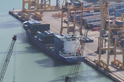 Photograph of a busy container port with cargo ships and cranes at sunset.